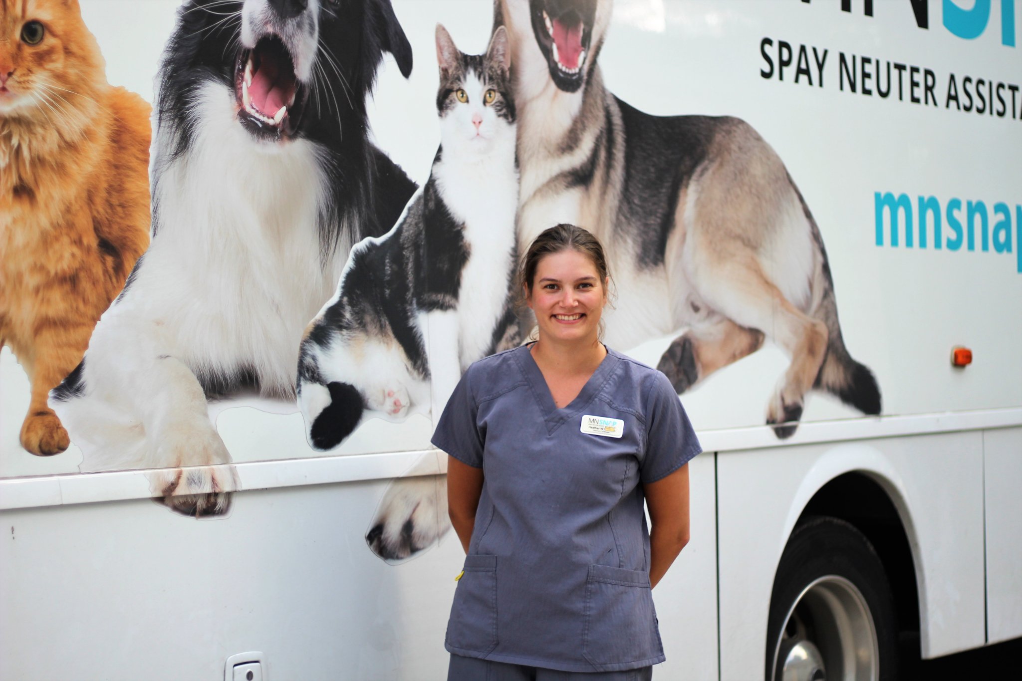 Smiling vet tech standing in front of a mobile surgery vet vehicle.